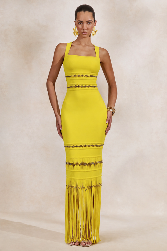 Woman wearing a yellow from allure dress with fringe details on a beige background