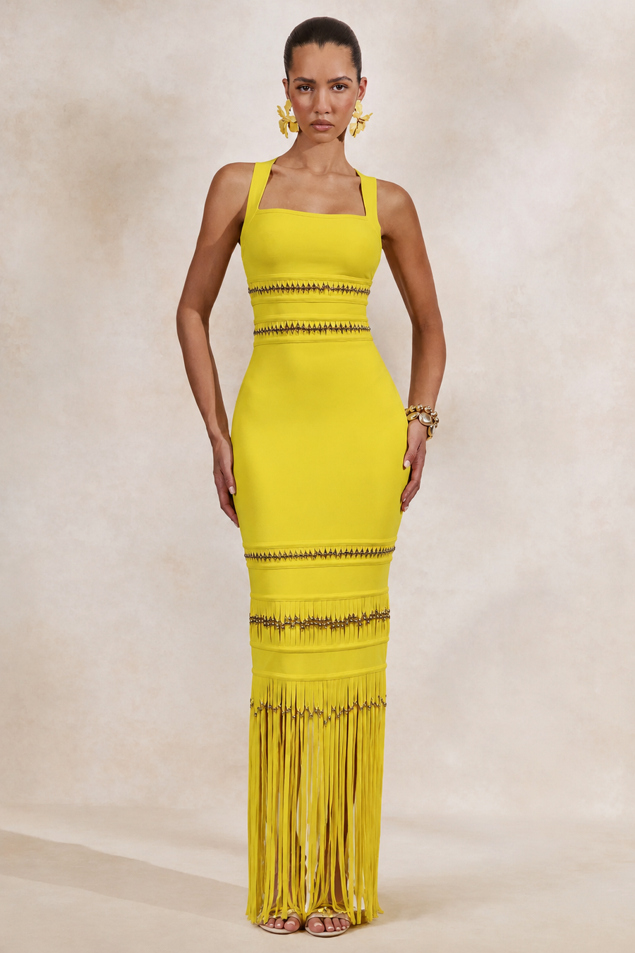 Woman wearing a yellow from allure dress with fringe details on a beige background