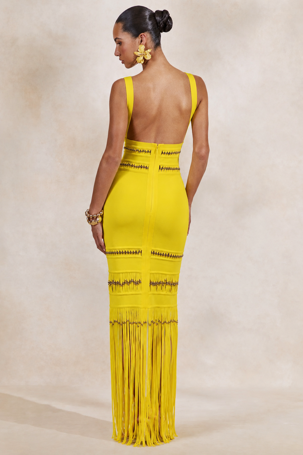 Woman wearing a yellow from allure dress with fringe details on a beige background